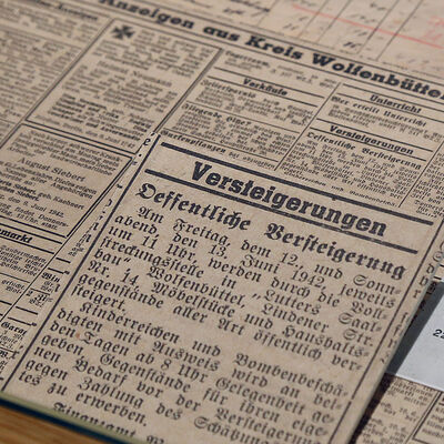 Das Foto zeigt einen Zeitungsausschnitt aus dem Jahr 1942. In der abgebildeten Anzeige wird eine Versteigerung angekündigt. Versteigert wurden im Juni 1942 unter anderem jüdische Möbel, Musikinstrumente, Teller und Gläser der deportierten Juden.