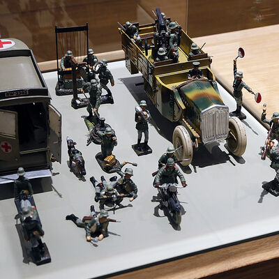Zu sehen ist Kriegsspielzeug unter einer Glasvitrine. Es handelt sich um grüne Plastiksoldaten der deutschen Wehrmacht und Panzerfahrzeuge, mit denen die Kinder Krieg spielten.