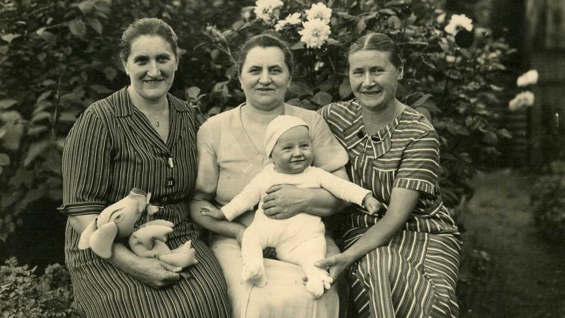 Zu sehen ist eine alte Schwarzweiß-Fotoaufnahme mit drei Frauen, einem Kind auf dem Schoß und ein Stofftier. Die linke Frau auf dem Bild ist Marie Deutschmann im Jahr 1936.