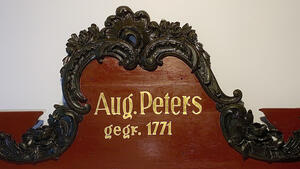 Ein geschnitzes Holzschild mit den Worten "Aug. Peters gegr. 1771". Es stammt aus dem 18. Jahrhundert.