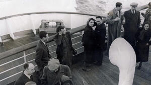 altes Schwarzweißfoto, an Deck eines großen Passagierschiffes aufgenommen, zeigt Männer und Frauen an Deck.