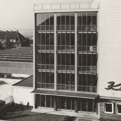 Schwarz-weiß-Fotografie. Das Gebäude im Vordergrund ziert der große Schriftzug »Kuba«. Links daneben ist ein Parkplatz zu erkennen