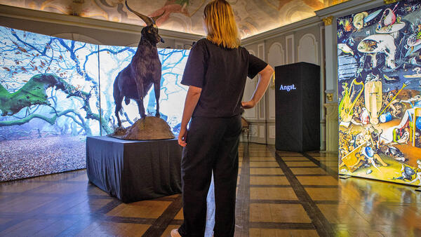 Eine Frau steht vor einem ausgestopften Ziegenbock, der als Exponat in einem Museum aufgestellt ist.