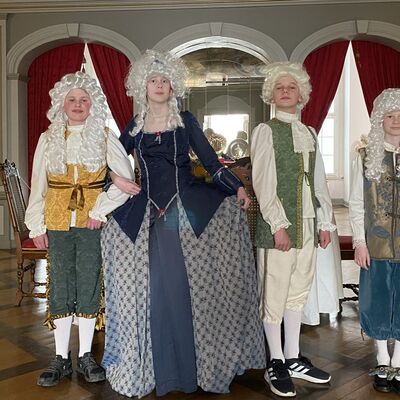 Vier in barocken Kostümen verkleidete Kinder stehen im Museum.