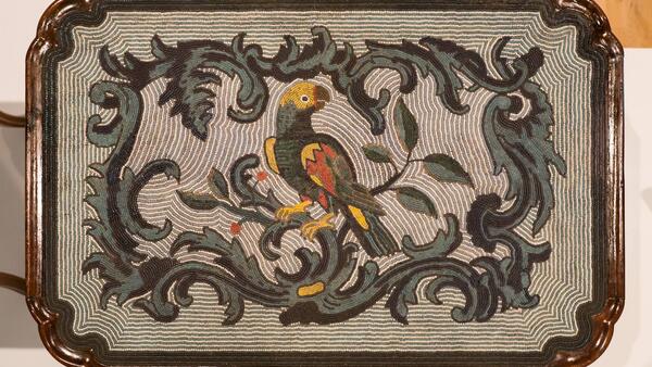 Eine mit farbigen Perlen besetzte Tischplatte mit Blätterranken und Papagei als Motiv