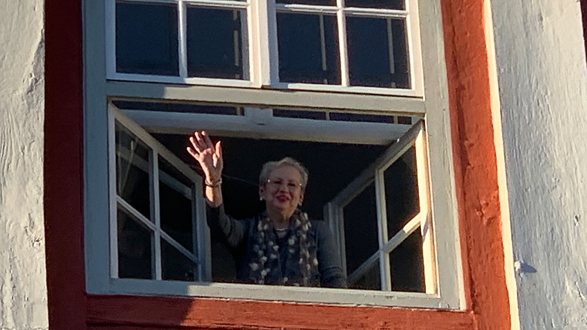 Eine Frau steht an einem Fenster und winkt.
